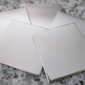 May include: Five silver metal squares, each with a smooth, polished surface. The squares are arranged in a staggered pattern, with the largest square in the center.