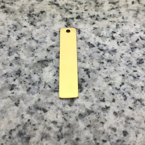Peut inclure: Une étiquette en métal de couleur dorée avec un trou en haut. L'étiquette est rectangulaire et a une surface lisse.