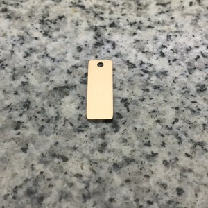 May include: A gold-colored metal tag with a hole at the top. The tag is rectangular and has a smooth surface.