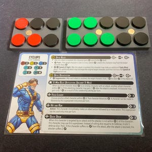 May include: A Cyclops character card from a tabletop game, with a blue and yellow illustration. Two gray trays hold red, black, and green game pieces. The card details Optic Blast, X-Men Blue, and other abilities.