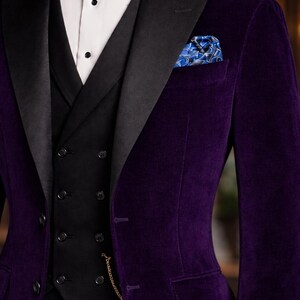 Puede incluir: Un conjunto formal con una blazer de terciopelo morado oscuro con solapas negras, un chaleco negro y una camisa blanca. Una pajarita negra y un pa&ntilde;uelo de bolsillo estampado a&ntilde;aden detalles. El traje tiene un corte cl&aacute;sico y entallado.