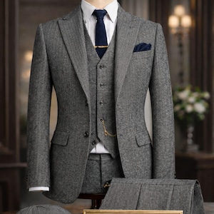 May include: A gray herringbone three-piece suit with a matching flat cap and trousers, displayed on a mannequin. The suit includes a white dress shirt, navy tie, and pocket square. A gold sign reads "THE NOBLE TAILOR" and "peaky blinder suit."
