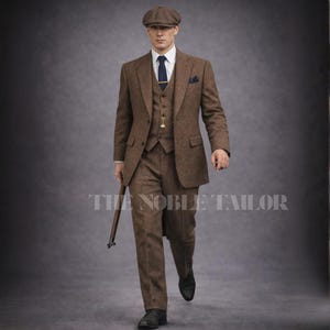 May include: A three-piece brown tweed suit with a matching flat cap, white shirt, and navy tie. The suit includes a blazer, vest, and trousers. A pocket square and a pocket watch are visible. The text "THE NOBLE TAILOR" is at the bottom.