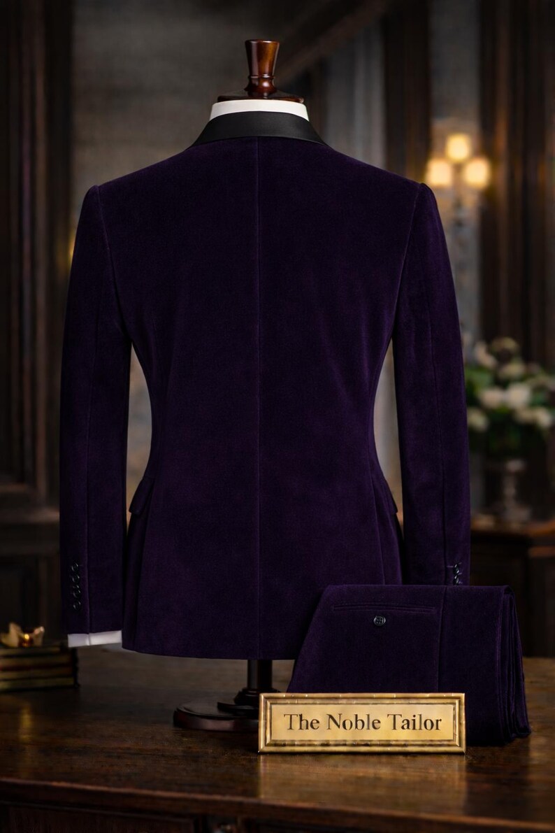 Puede incluir: Un traje formal de terciopelo morado expuesto en un maniqu&iacute;. El traje incluye una chaqueta con solapa de sat&eacute;n negro y pantalones a juego. El letrero frente al traje dice "The Noble Tailor".