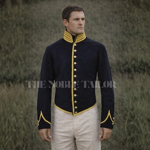 Könnte beinhalten: Marineblaue Jacke mit goldfarbenen Verzierungen und Knöpfen. Die Jacke hat einen hohen Kragen und lange Ärmel. Der Text "THE NOBLE TAILOR" ist auf der Vorderseite aufgedruckt. Die Person trägt eine cremefarbene Hose.