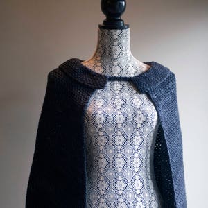 Puede incluir: Un chal de punto azul oscuro con cuello, exhibido en un maniquí cubierto de encaje blanco.
