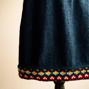 Könnte beinhalten: Ein dunkelblauer Strickrock mit einem bunten bestickten Saum. Der Rock ist aus einem weichen, strukturierten Stoff gefertigt und hat ein schlichtes, klassisches Design.