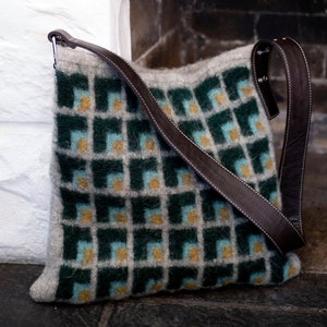 Könnte beinhalten: Eine gestrickte Tasche mit grünem, blauem und beigefarbenem Muster und einem braunen Lederriemen.