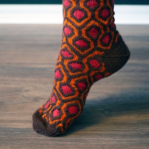 May include: A brown and orange sock with a pink honeycomb pattern. The sock is knitted and has a ribbed cuff.