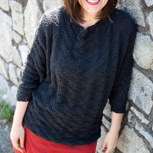 May include: A woman wearing a dark gray knitted sweater with a red corduroy skirt and black tights. She is smiling and wearing glasses.