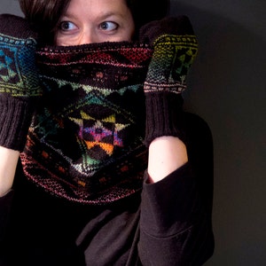 May include: A person wearing a black sweater with a colourful knitted cowl neck and matching fingerless gloves.