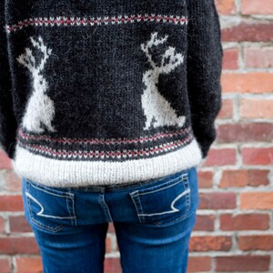 Könnte beinhalten: Ein schwarzer Pullover mit einem weißen Rentiermuster. Der Pullover hat einen weißen Bund unten und einen roten und weißen Bund oben.