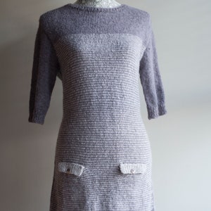 Könnte beinhalten: Ein graues und weiß gestreiftes Strickkleid mit zwei Taschen auf der Vorderseite. Das Kleid hat einen runden Ausschnitt und Dreiviertelärmel.