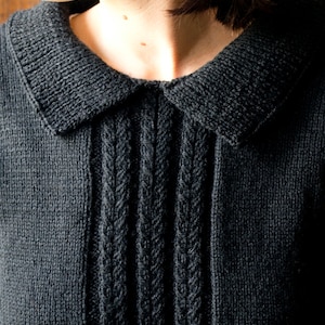 May include: A close-up of a black knitted sweater with a cable knit design and a collar.