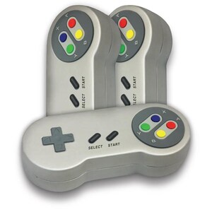 May include: Three gray retro-style video game controllers. Each controller has a directional pad, select and start buttons, and colored buttons. The controllers are designed to resemble a classic console controller.