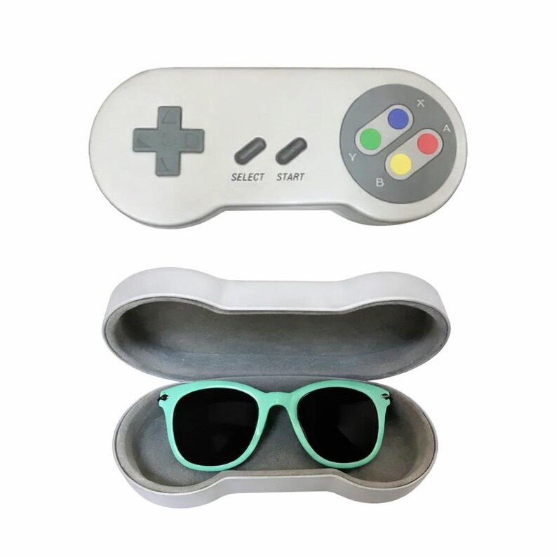 May include: A white sunglasses case shaped like a retro video game controller, with a pair of mint green sunglasses inside. The controller case has a gray directional pad, buttons, and the words "SELECT" and "START".