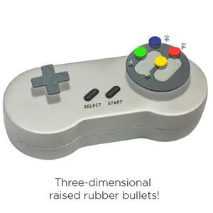 May include: A light gray retro video game controller with a directional pad, select and start buttons, and colored action buttons. The text "Three-dimensional raised rubber bullets!" is at the bottom.