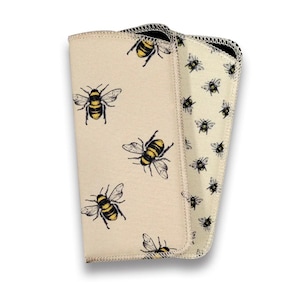 May include: A folded, cream-coloured cloth featuring a repeating pattern of black and yellow bees. The cloth has a contrasting black border and a second layer with a smaller bee pattern.