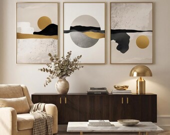 Puede incluir: Tres impresiones artísticas abstractas enmarcadas con marcos dorados. Cada impresión presenta un diseño de paisaje minimalista con tonos dorados, negros y neutros. La obra de arte cuelga sobre un mueble de madera oscura, un sillón beige y una mesa de centro de mármol.