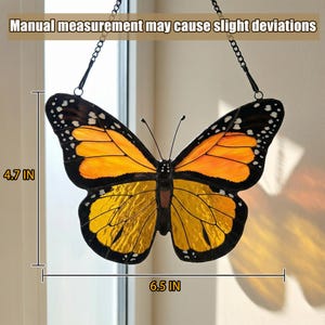 K&ouml;nnte beinhalten: Glasmalerei-Schmetterling-Suncatcher, 16,5 cm breit und 12 cm hoch. Der Schmetterling hat orange und gelbe Fl&uuml;gel mit schwarzen R&auml;ndern und wei&szlig;en Punkten. Er h&auml;ngt an einer schwarzen Kette. Text: Manuelle Messung kann leichte Abweichungen verursachen.
