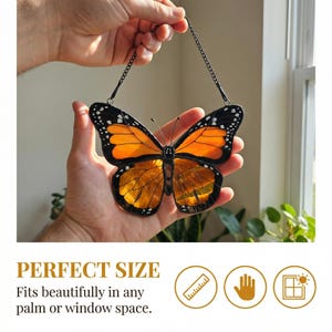 K&ouml;nnte beinhalten: Ein Buntglas-Schmetterling mit orangefarbenen und schwarzen Fl&uuml;geln, der an einer Kette h&auml;ngt. Der Schmetterling wird vor einem Fenster pr&auml;sentiert. Der Text "PERFECT SIZE" ist sichtbar. Der Schmetterling hat ein detailliertes Muster.