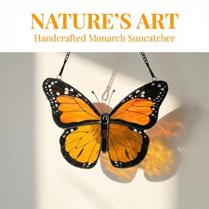 K&ouml;nnte beinhalten: Ein handgefertigter Monarchfalter-Sonnenf&auml;nger mit orangefarbenen und schwarzen Fl&uuml;geln, wei&szlig;en Punkten und einem schwarzen Rand. Der Text "NATURE'S ART Handcrafted Monarch Suncatcher" steht oben. Der Sonnenf&auml;nger h&auml;ngt an einer Kette.