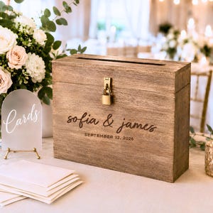 May include: A rectangular wooden card box with a slot on top and a gold padlock. The front is engraved with the text "sofia & james" and "SEPTEMBER 12, 2026". Beside it stands an arched frosted acrylic sign with the white text "Cards".
