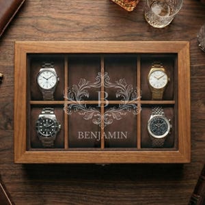May include: A wooden watch display case with six compartments, each holding a wristwatch. The case is personalized with the name "Benjamin" and an ornate initial. Other items on the wooden surface include a leather cigar case, a lighter, and a bottle of liquor.