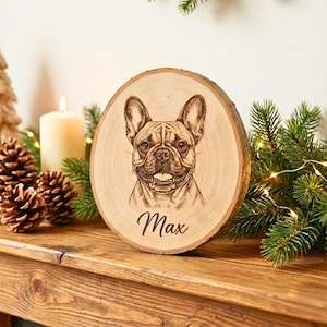 May include: A round wooden plaque with a detailed engraving of a French Bulldog's face. The dog's name, "Max," is written in cursive below the image. The plaque is displayed on a wooden surface with festive decorations.