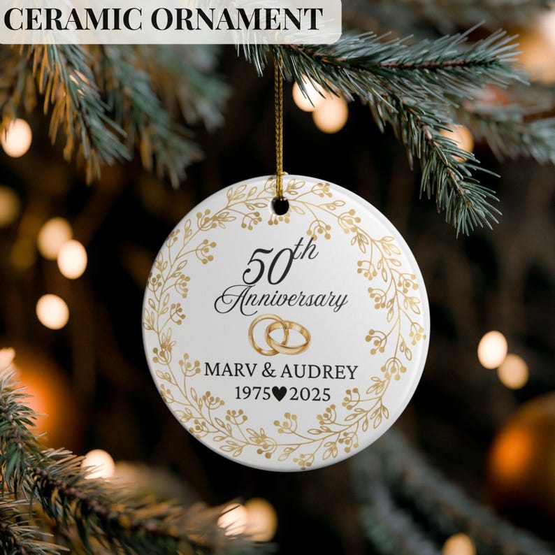 May include: White ceramic ornament with gold accents, featuring the text "50th Anniversary" and the names "Marv & Audrey" with the years "1975-2025". The ornament is round and has a gold string for hanging.
