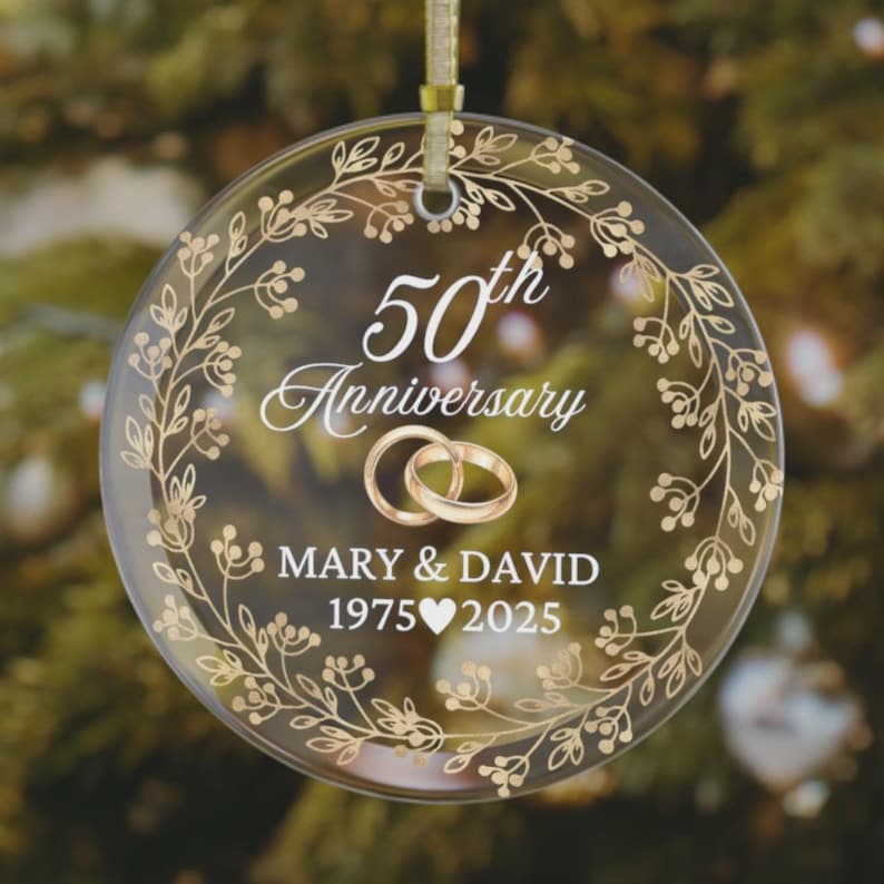 Golden 50th Anniversary Ornament personalized with couple names “Mary & David” and wedding years 1975–2025, clear glass keepsake with gold floral wreath design and interlocking rings, elegant custom gift for parents or grandparents celebrating their golden anniversary.