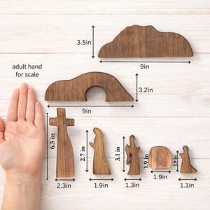 May include: Wooden Easter scene set with a cross, figures, and a tomb. The largest piece is 9 inches wide. The set includes a cross, a figure, an angel, and a tomb. The pieces are made of stained wood and are displayed on a light wood surface.