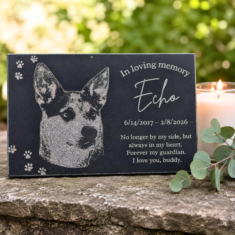 Personalized dog memorial gift — black granite pet memorial stone engraved with a photo of a dog named Echo, "In loving memory," with paw prints, a candle, and eucalyptus in a garden.