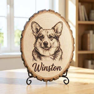 May include: A wooden plaque featuring a detailed pyrography portrait of a Corgi dog. The dog's name, "Winston," is elegantly burned into the wood beneath the image. The plaque is displayed on a black metal stand, showcasing the natural wood grain.