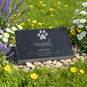 K&ouml;nnte beinhalten: Ein rechteckiger Gedenkstein f&uuml;r Haustiere aus schwarzem Stein mit einer eingravierten Pfote, dem Namen "rascal", den Jahren "2012-2019" und dem Text "YOU LEFT A PAW PRINT ON OUR HEARTS" auf der polierten Vorderseite des Steins.