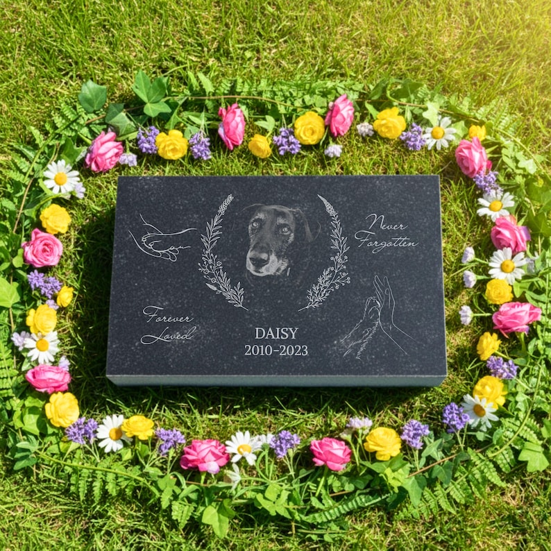 K&ouml;nnte beinhalten: Eine rechteckige Gedenktafel aus schwarzem Granit mit einem eingravierten Hundeportr&auml;t, das von einem Blumenkranz umgeben ist. Der Text lautet "Forever Loved", "DAISY", "2010-2023" und "Never Forgotten", erg&auml;nzt durch Strichzeichnungen von H&auml;nden.