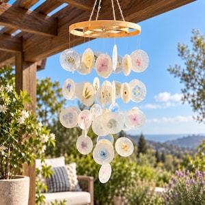 May include: A hanging mobile featuring a circular wooden frame with multiple translucent, circular discs suspended by thin threads. Each disc contains a pressed, dried flower in various colors including pink, blue, yellow, and white.