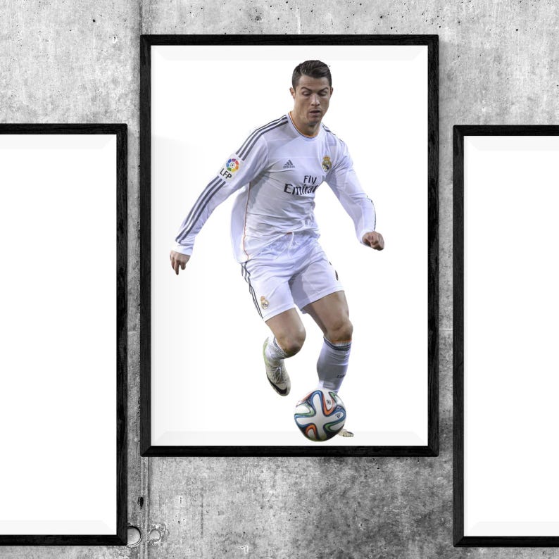 May include: Framed print featuring a soccer player in a white uniform, dribbling a soccer ball. The player is in action, with a focused expression. The print is set against a white background, framed in black.