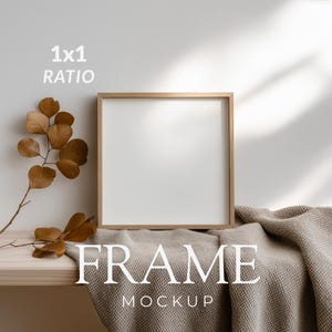 Pode incluir: Uma moldura quadrada de madeira com um centro branco vazio. A moldura está posicionada ao lado de um ramo de eucalipto seco castanho e um tecido bege texturizado. O texto 1x1 RATIO e FRAME MOCKUP é visível em letras brancas.