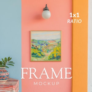 May include: A square wooden frame containing a landscape painting of rolling green hills and yellow foliage, mounted on a coral-colored wall below a white globe wall lamp. The text 1x1 RATIO and FRAME MOCKUP are printed in white on the wall.