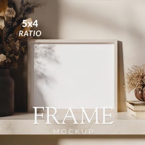 Pode incluir: Uma moldura retangular de cor clara com um centro branco vazio, posicionada numa prateleira. A moldura apresenta o texto 5x4 RATIO e FRAME MOCKUP. À esquerda, um vaso escuro com flores secas e, à direita, livros empilhados.