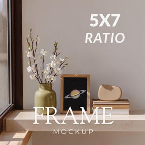 May include: A wooden frame mockup with a black background and a Saturn graphic. The frame is displayed on a shelf with a vase of white flowers, a beige vase, and a stack of books. The text "5X7 RATIO" and "FRAME MOCKUP" are visible.