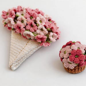May include: A crochet bouquet of pink and light pink flowers arranged in a cream-colored cone, accompanied by a small, round crochet flower arrangement featuring shades of pink and red flowers set in a brown, textured, basket-like base.