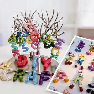 May include: A display of colorful, handmade crochet keychains and letters. The keychains are in the shape of numbers and whimsical figures. The letters spell out "DIY CRAFT". The keychains hang from a silver tree-shaped display.