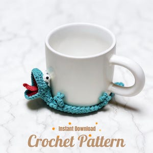 May include: A white ceramic mug with a teal crochet lizard coaster. The lizard has a red tongue and white eyes. The words "Instant Download" and "Crochet Pattern" are in the image.