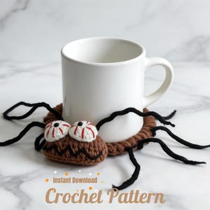May include: A white ceramic mug rests on a brown crocheted spider coaster with black legs and googly eyes. The coaster has a brown body with white and red eyes. Text at the bottom reads "Instant Download Crochet Pattern".