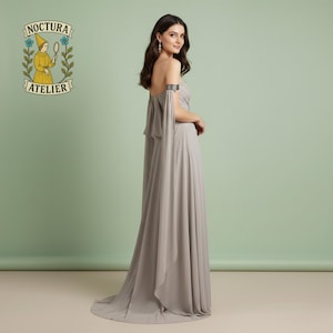 May include: A floor-length, strapless taupe gown featuring a flowing, layered bodice and long, detached chiffon sleeves that drape from the upper arms. The dress includes a metallic silver arm cuff on the left arm and a subtle train at the hem.