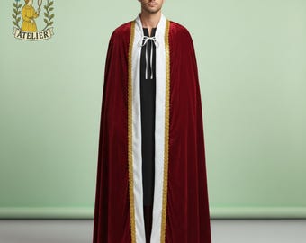 May include: A burgundy velvet cloak with gold trim and a white center panel. The cloak is worn over a black garment. The image includes the "Noctura Atelier" logo in the upper left corner. The cloak is a full-length garment.