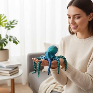 May include: A blue and green octopus figurine with textured details. The octopus has a rounded head and long, segmented tentacles. The figurine is held in someone's hands.
