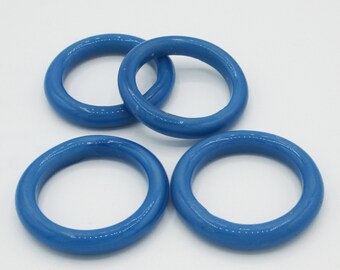 May include: Four glossy, blue, circular bangles are arranged on a white surface. The bangles are a solid, medium blue color and appear to be made of a smooth material. The bangles are evenly spaced and slightly overlapping.